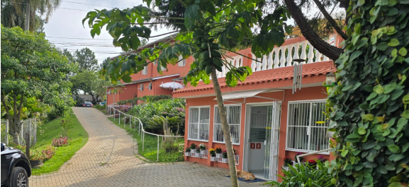 Imagem frontal da Clínica Portal 8. Uma casa rosada, com um caminho entre jardins, e um céu azulado com nuvens.